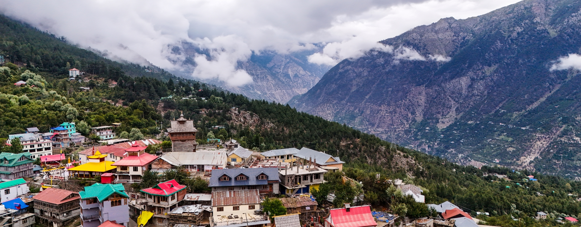 Scenic mountain village view showcasing one of the offbeat places in Himachal with colorful houses, pine forests, and misty Himalayan valleys